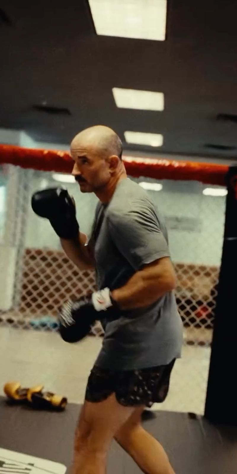 Chris Petkas shadowboxing in gloves beside the cage at an MMA gym